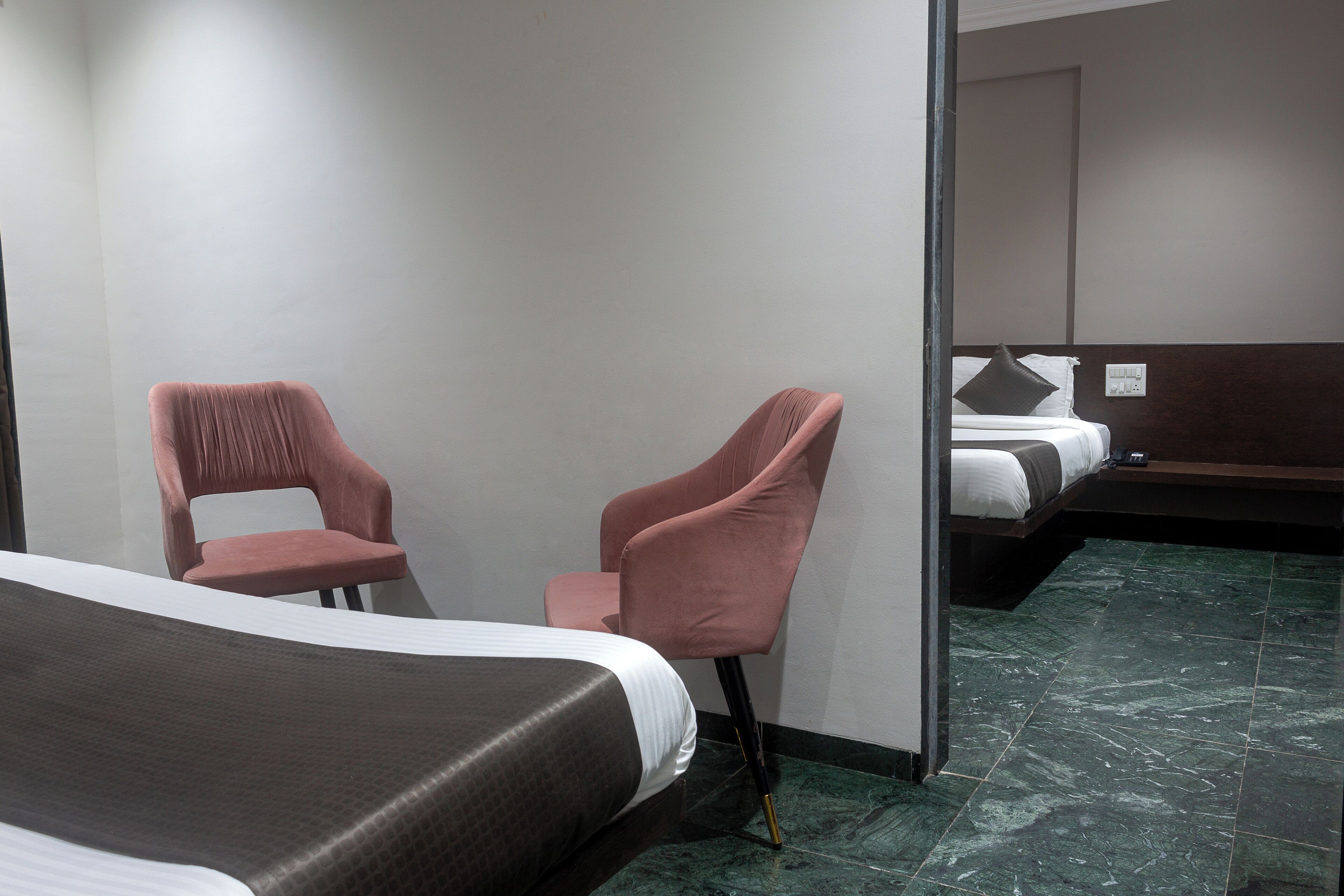 A hotel room with a bed, two pink chairs, a small table, and a mirror.