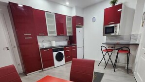 A compact kitchen with red and white cabinets, a microwave, a washing machine, and a dining area with a red table and chairs. - Apartmen with Gym 20 min from the center of Madrid (Leganés)