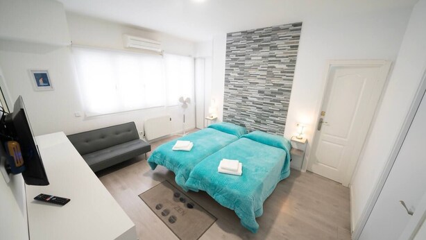 A modern hotel room with a sofa, two beds with towels, a desk, a TV, and a wall with a textured pattern. - Apartmen with Gym 20 min from the center of Madrid (Leganés)