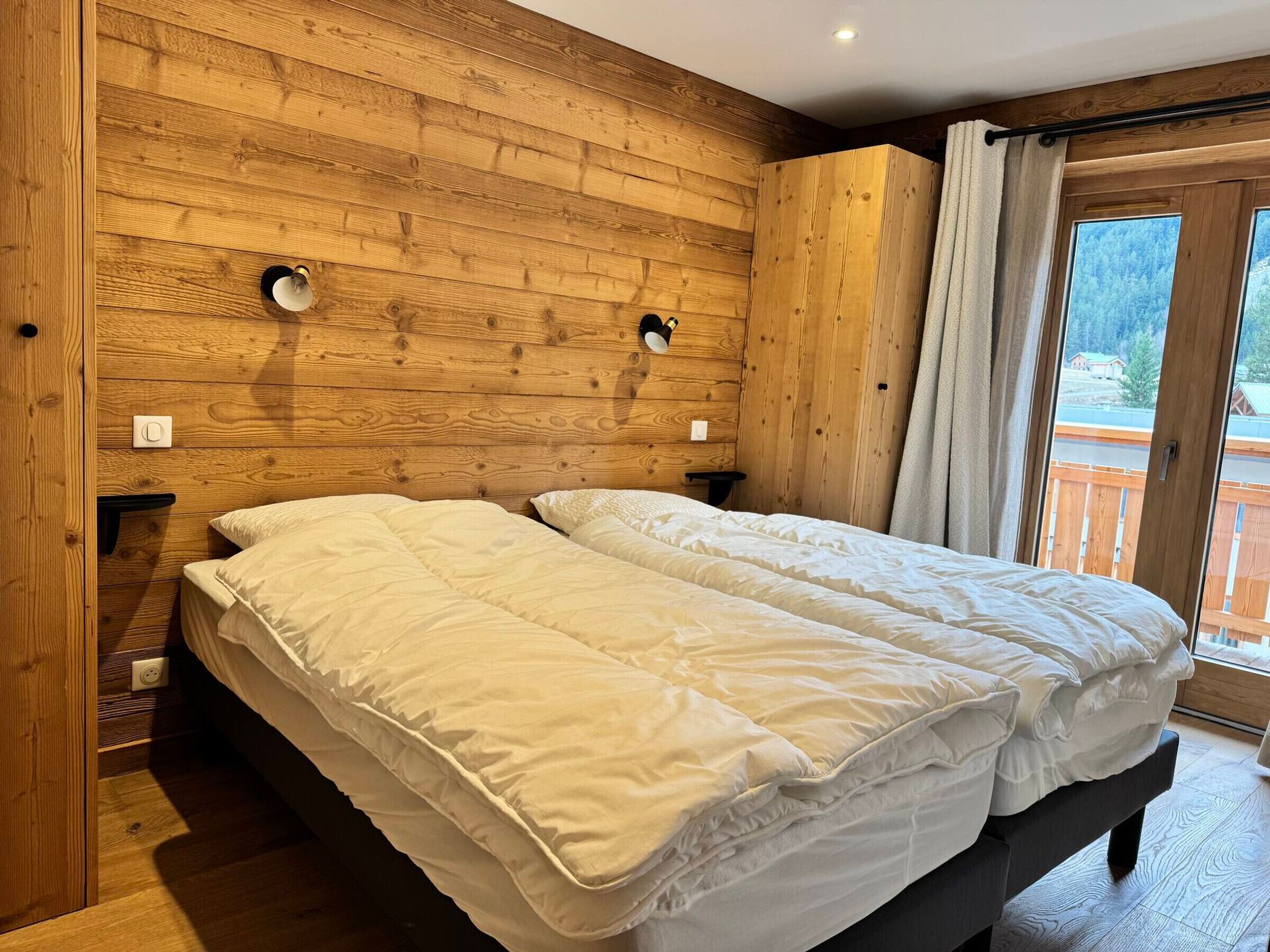Una habitación con paneles de madera, una cama, dos mesitas de noche y un ventanal con cortinas.