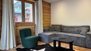 Una sala de estar moderna con un sofá modular, un sillón verde, una pequeña mesa redonda y un tapete de cuero de vaca blanco y negro.