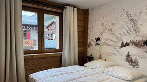 Un dormitorio con cama, ventana con cortinas, un mural de montañas y un cartel que dice "POSTALE".