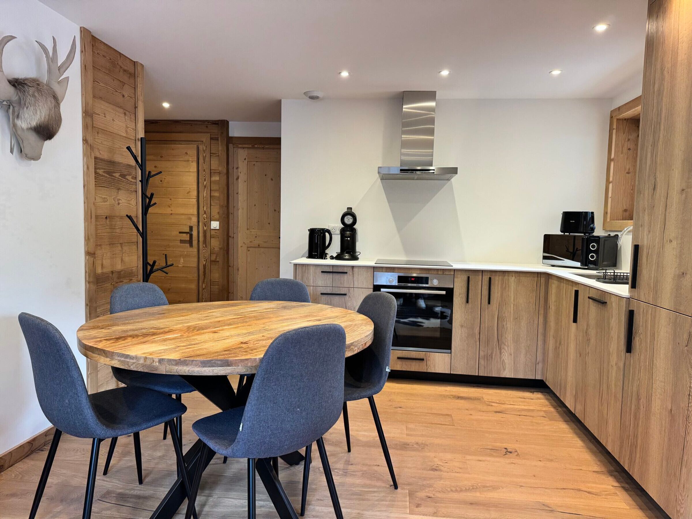 Een moderne keuken met een ronde houten tafel, blauwe stoelen en houten kastjes.
