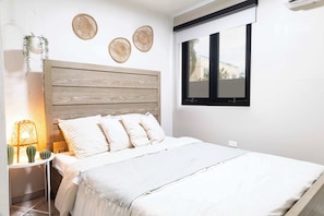 A bedroom with a wooden headboard, white bedding, a bedside table with a lamp, and wall decor. - Entire complex  Beachfront Villa Complex 12 Bedrooms, 6 Baths, Sleeps 48 (Dorado)