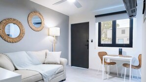 A modern living room with a sofa, two round mirrors, a lamp, a dining table with chairs, and a window with a view.