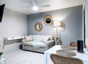A modern living room with a grey sofa, a white coffee table, a floor lamp, and two wall-mounted mirrors.