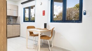 Pieni ruokailutila, jossa on pöytä ja tuolit, keittiö, jossa on sisäänrakennettu uuni, sekä suuret ikkunat, joista avautuu näkymä puita kohden.