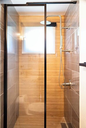 Una ducha con cerramiento de vidrio, suelo de madera y paredes de azulejos.