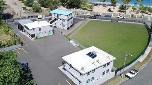 Vista aérea de un complejo de edificios con estacionamiento, zona verde y vista al océano.