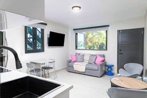 A modern living room with a sofa, a TV, a dining area, and a kitchen.