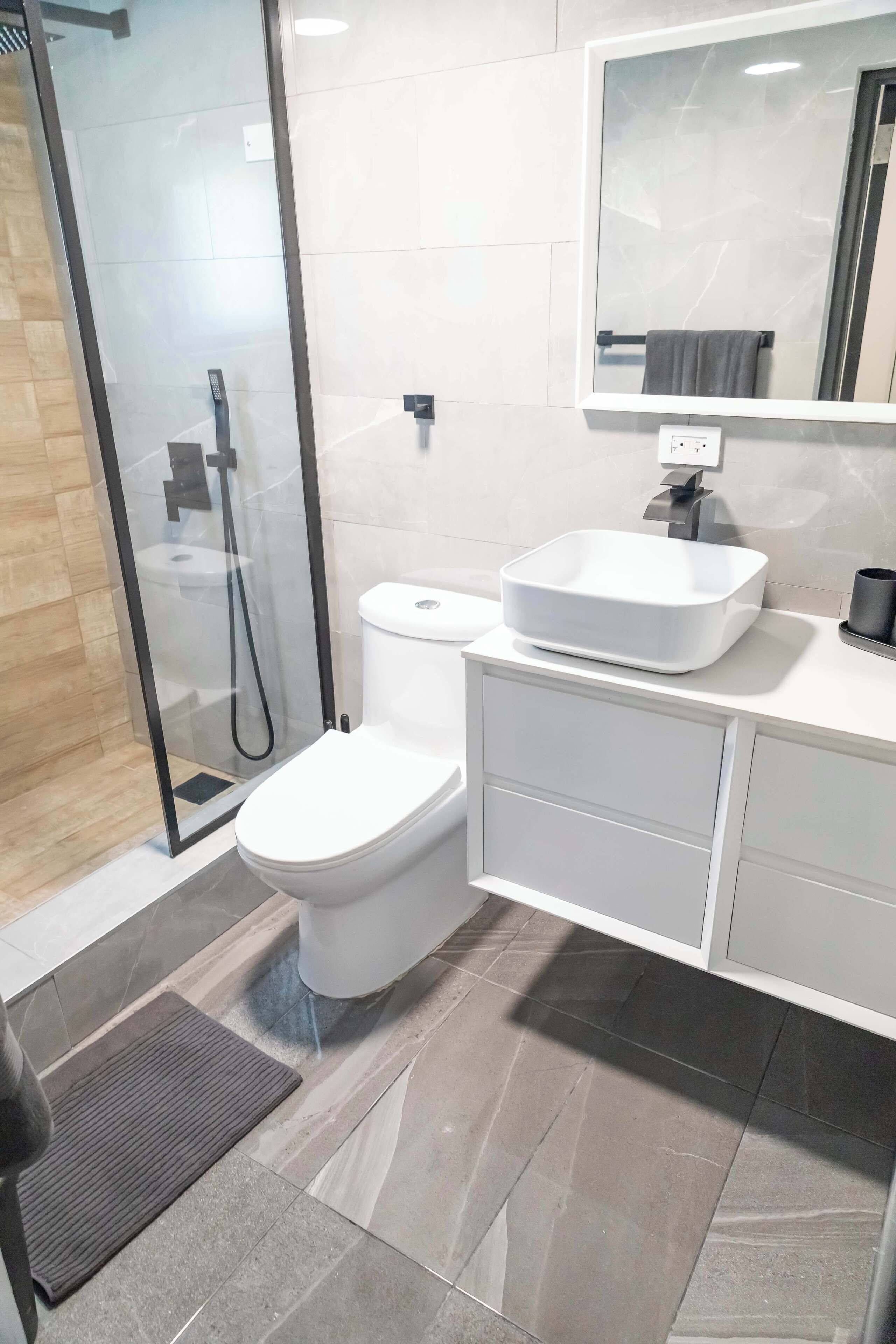 Un baño moderno con ducha de vidrio, inodoro blanco y tocador con un espejo grande.