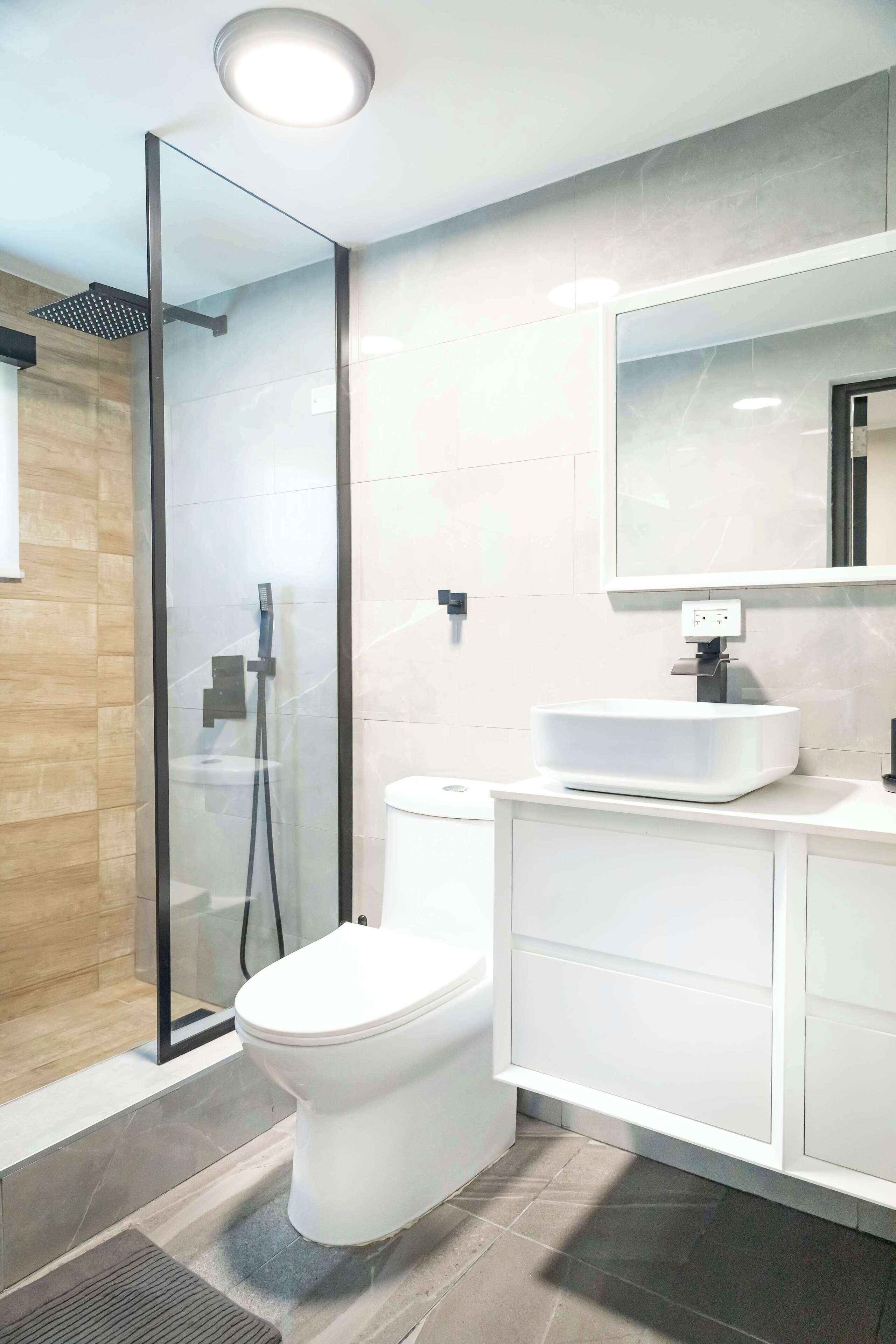 Un baño moderno con ducha envuelta en vidrio, un inodoro blanco y un tocador con espejo.
