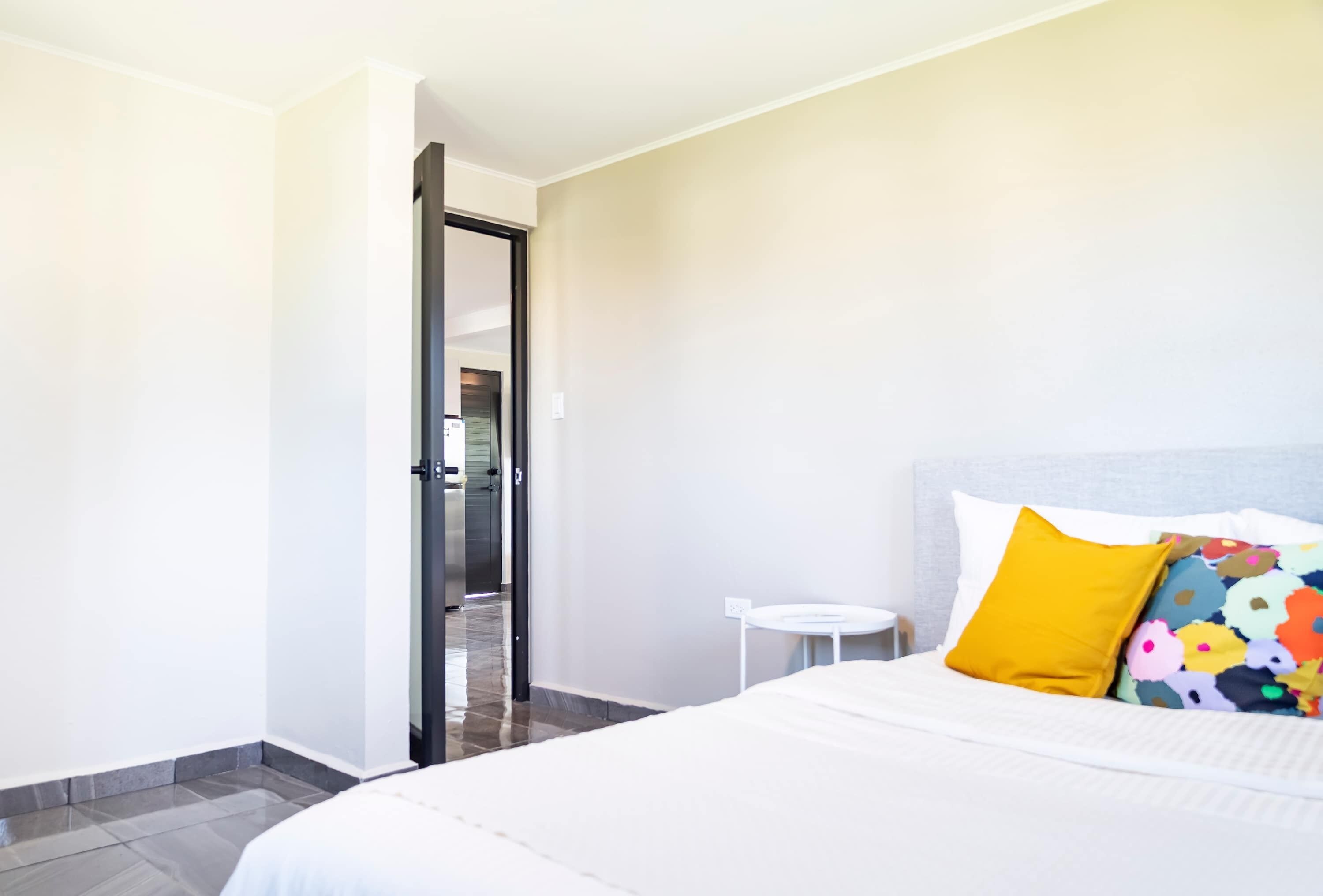 A hotel room with a bed, a small round table, and a door leading to a hallway.