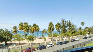 A beachside parking area with cars, palm trees, and a view of the ocean.