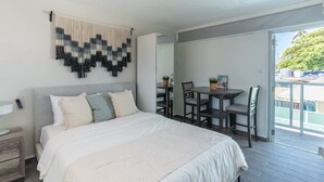 A bedroom with a bed, bedside table, and a dining area with chairs and a table. - AQUA Terrazas 4+5 · Oceanfront Duo Retreat w Pool (Dorado)