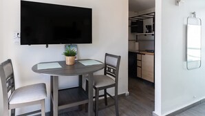 A modern living room with a flat-screen TV mounted on the wall, a round dining table with two chairs, and a small potted plant on the table. - AQUA Terrazas 4+5 · Oceanfront Duo Retreat w Pool (Dorado)