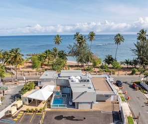 A hotel with a rooftop pool, a parking area, and a view of the beach and ocean.