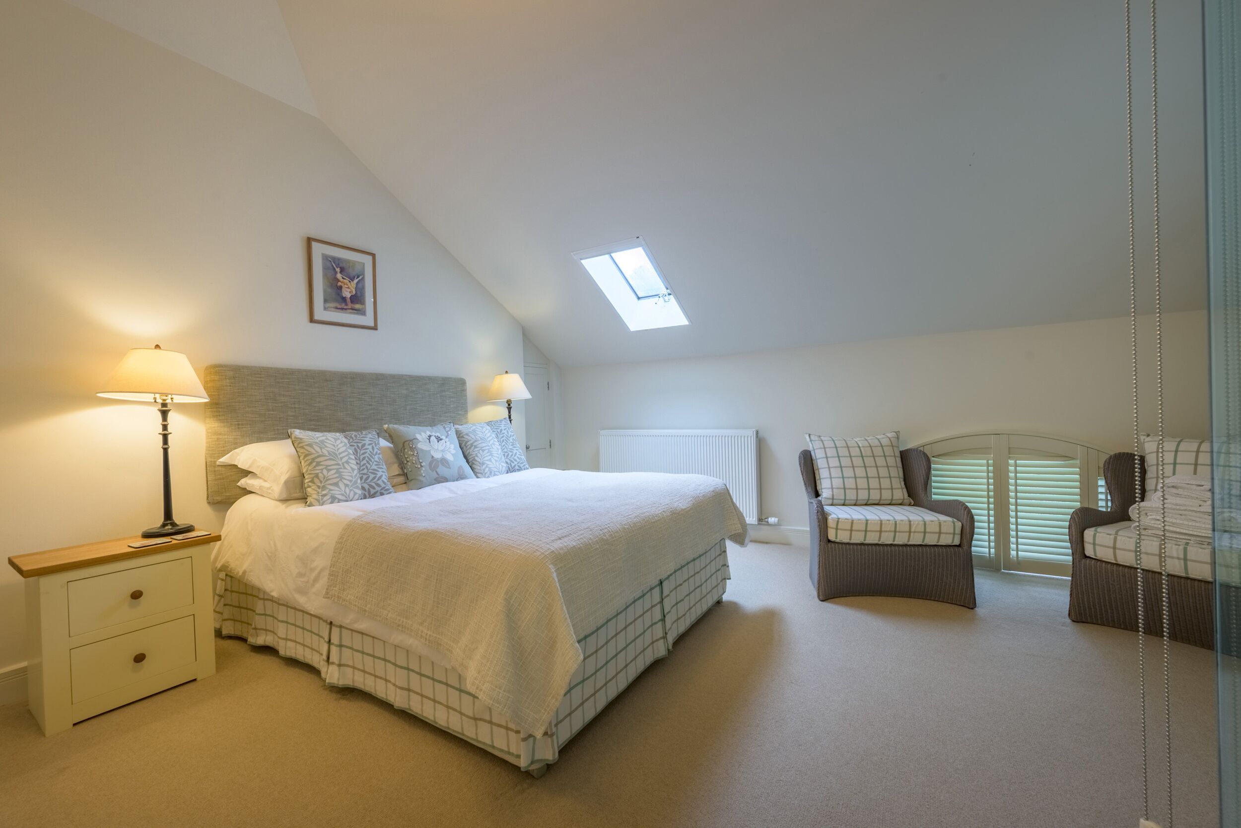 A bedroom with a large bed, a nightstand, a lamp, a window, and two chairs.