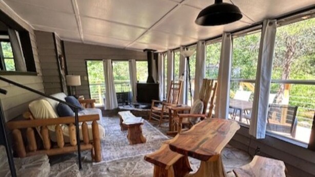A spacious room with a stone floor, wooden furniture, and large windows offering a view of greenery. - NEW LISTING:Spring River:Creek Cabin, Private Footage on South Fork Spring River (Hardy)
