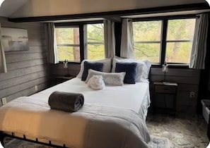 Une chambre Ă coucher avec un lit, deux tables de chevet, une fenĂȘtre avec des rideaux et un tableau au mur.