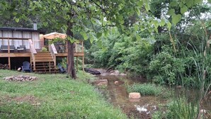 A wooden deck with outdoor seating, a small bridge over a stream, and a forested backdrop. - NEW LISTING:Spring River:Creek Cabin, Private Footage on South Fork Spring River (Hardy)