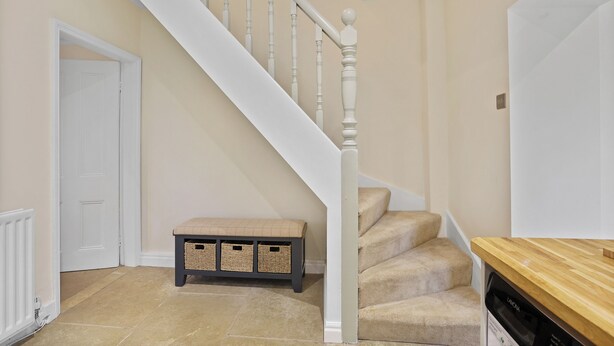 Eine Treppe mit weißen Balustraden, Teppichstufen in Beige und eine Holzbank mit Körben.