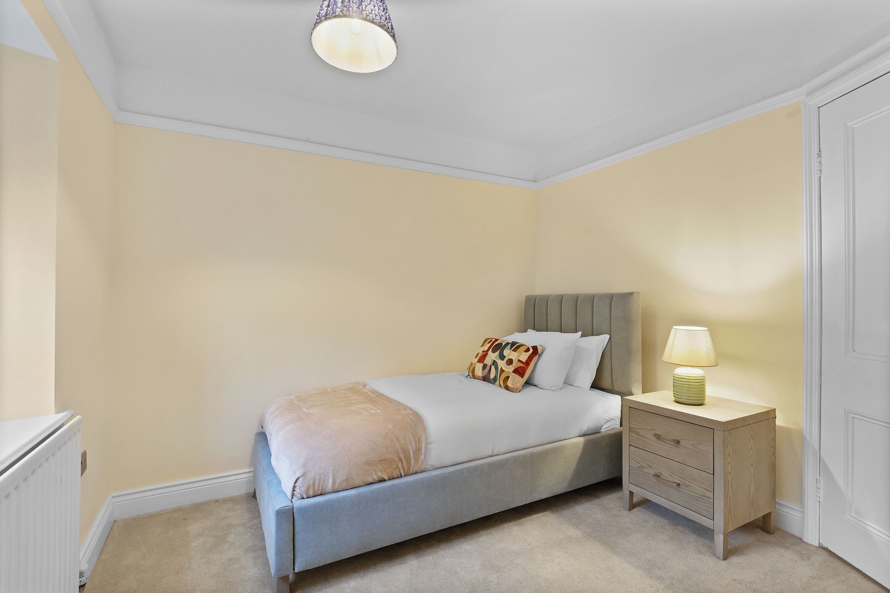 A bedroom with a bed, bedside table, lamp, and a radiator.