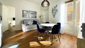 A modern living room with a white sofa, blue chairs, a round table, and a decorative wall piece.