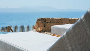 Een uitzicht op zee met een stenen muur, houten omheining en ligstoelen.