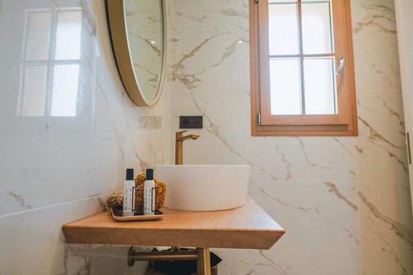 A bathroom with a marble wall, a wooden vanity, a white sink, and a window with wooden frames.
