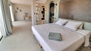 Une chambre à coucher avec un grand lit, une table de chevet, une armoire et une salle de bain visible à travers une arche.