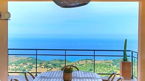 Une table et des chaises en bois sur un balcon offrant une vue sur la mer et les collines.