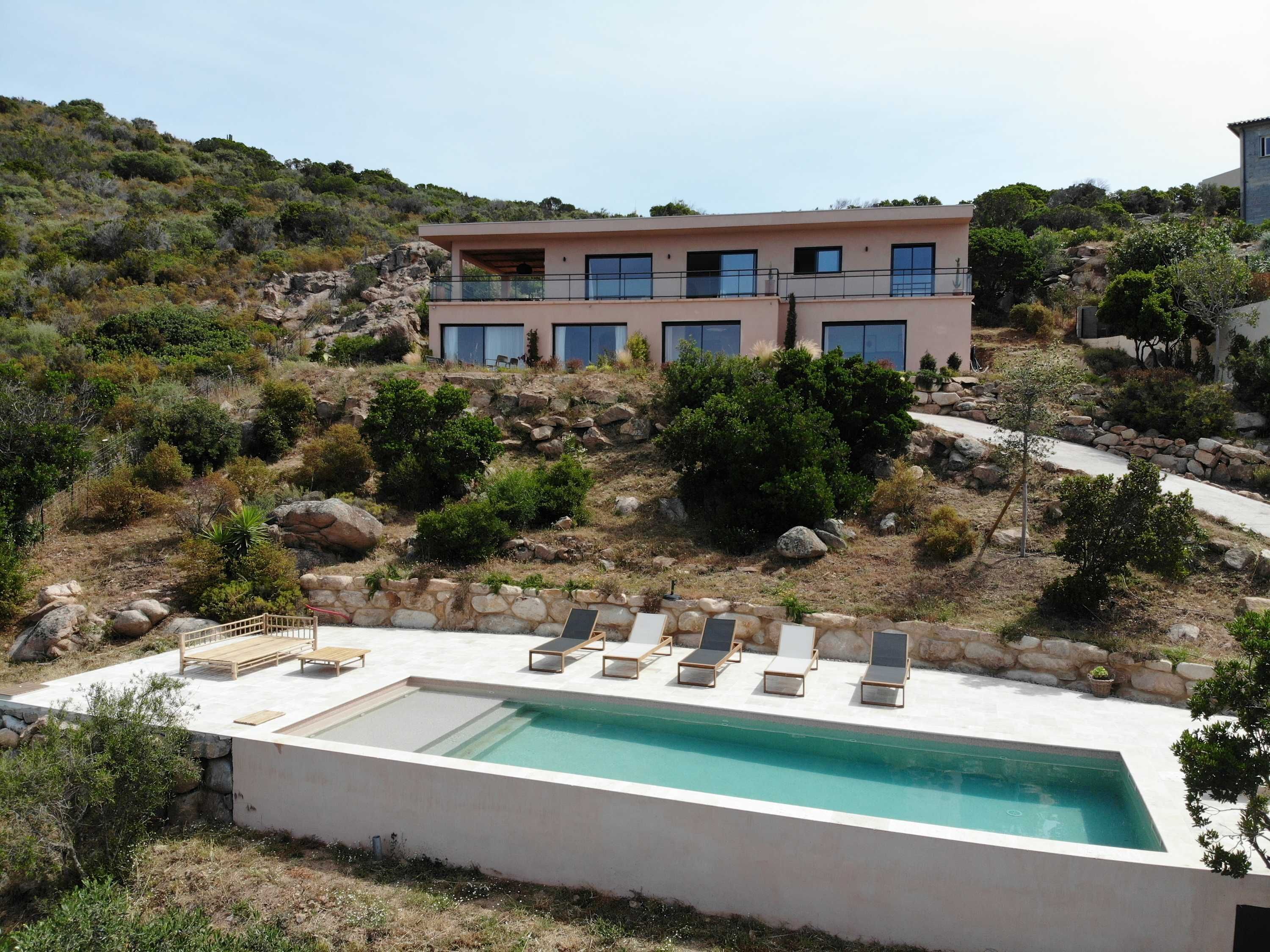 Ein modernes Haus mit Pool, umgeben von natürlicher Landschaft und felsigem Gelände.