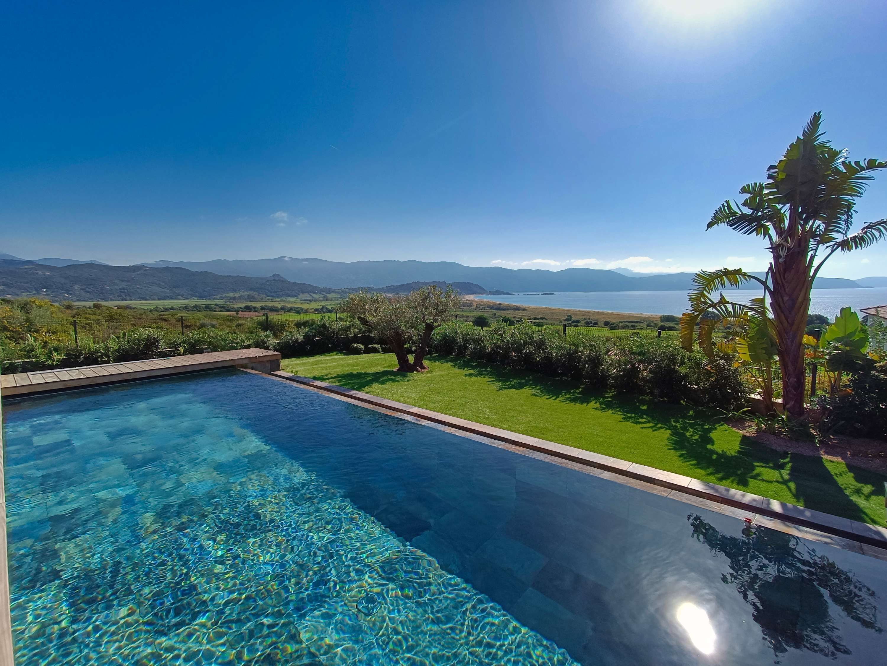 A clear blue swimming pool with a view of mountains and a grassy landscape.