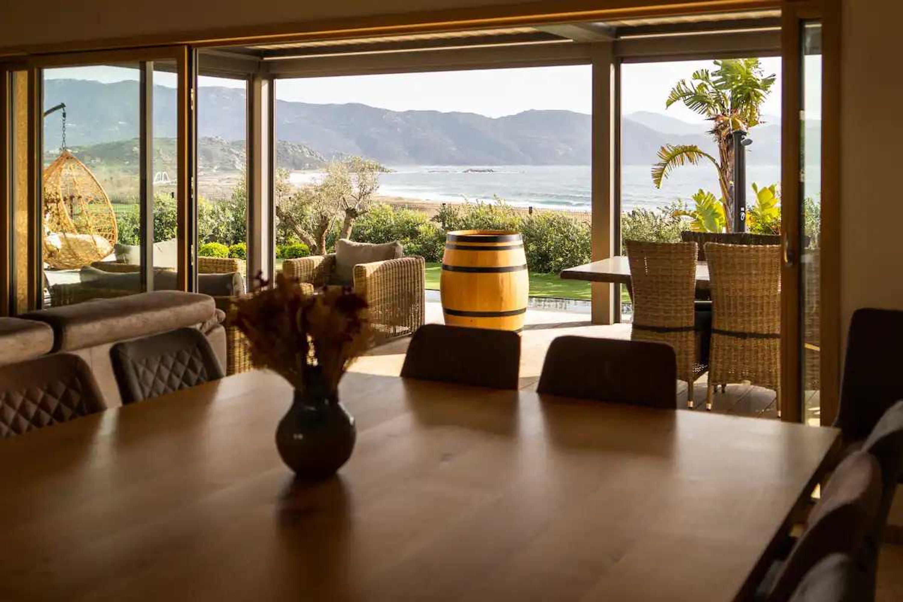 Un comedor con mesa de madera, sillas de mimbre y vista al océano y las montañas.