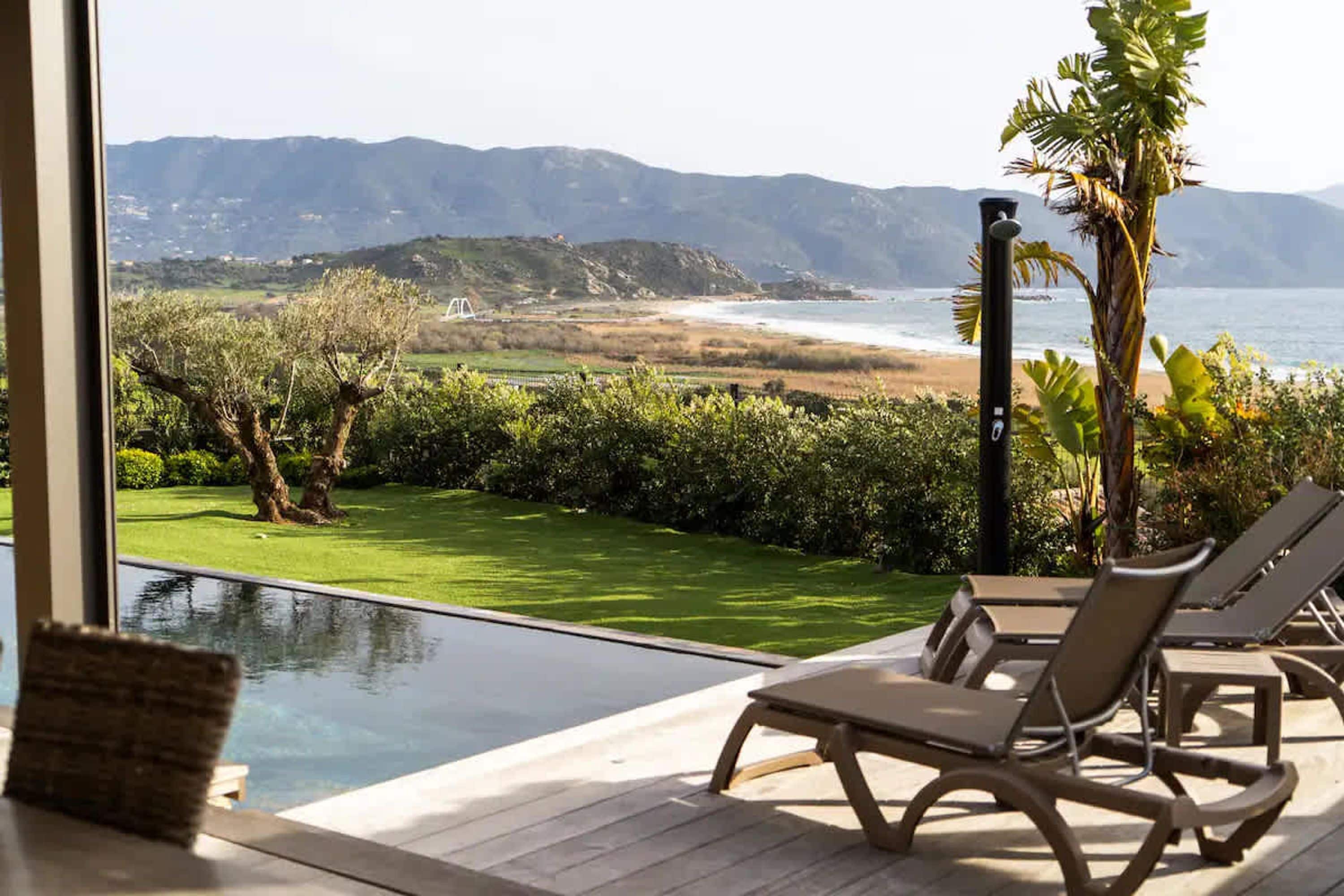 Ein Poolbereich mit Liegestühlen und Blick auf Strand und Berge.