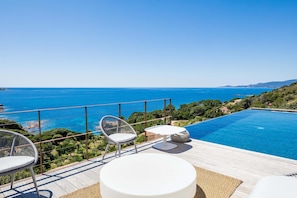 A rooftop terrace with a pool, chairs, and a table overlooking a coastal landscape.
