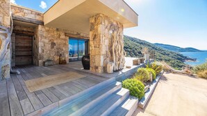 A modern building with stone walls, a wooden deck, and a view of the sea. - Architect Villaproperty Sea View Close to the Beaches (Calcatoggio)