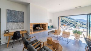 A modern living room with a fireplace, seating area, and a large window offering a view of the outdoors. - Architect Villaproperty Sea View Close to the Beaches (Calcatoggio)