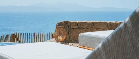 A seaside view with a stone wall, wooden fence, and lounge chairs.