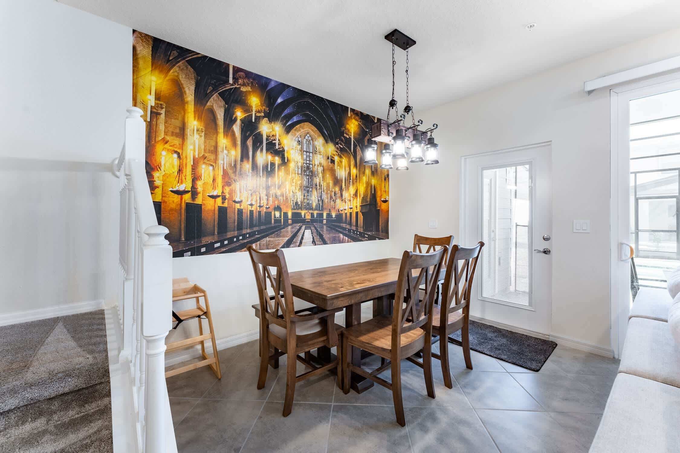 Un espace repas comprenant une grande table et des chaises, un lustre et une fresque murale.