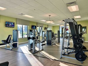 Ein Fitnessstudio mit unterschiedlichen Trainingsgeräten, großen Fenstern und einem Fernseher an der Wand.