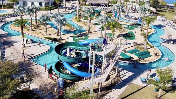 Un parc aquatique doté de plusieurs piscines, de toboggans et d’espaces de détente, le tout entouré de palmiers et de bâtiments.