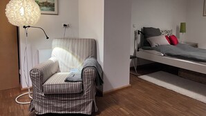 A room with a striped armchair, a bed with pillows, a floor lamp, and a painting on the wall.