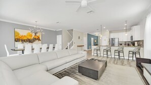 A modern living room with a sectional sofa, a coffee table, and a dining area with chairs and a chandelier. - South Pool | Game Room | Waterpark | Disney 9036 (Four Corners)