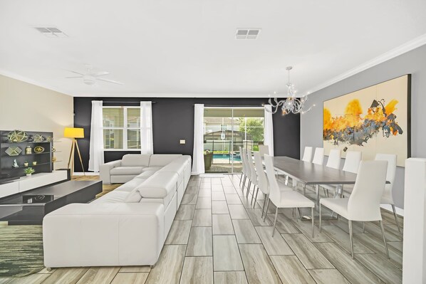 Un salon moderne avec un canapé d’angle, une table à manger avec des chaises et un grand tableau abstrait accroché au mur.