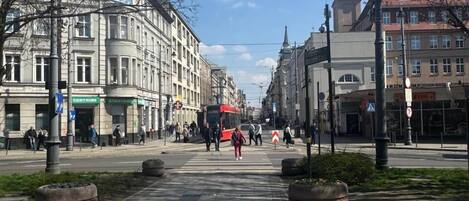 A spacious square with a central pedestrian crossing, surrounded by historic buildings and a red bus in the distance.