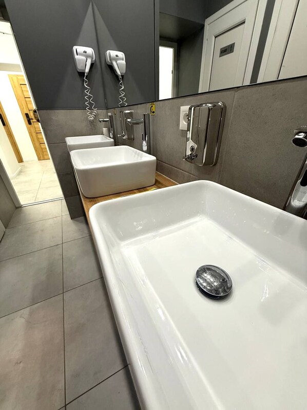 A modern bathroom with a large white bathtub, two white sinks, and a hairdryer mounted on the wall. - Green Hostel Katowice (Katowice)