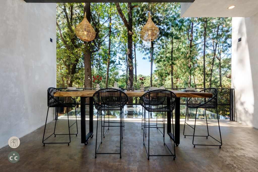 An outdoor dining area with a long wooden table and four black chairs, surrounded by trees and a glass railing.