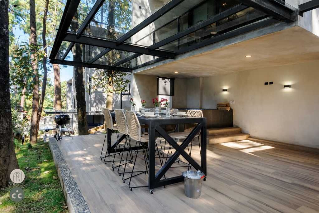 A modern outdoor dining area with a glass ceiling, a grill, and a dining table set for four.